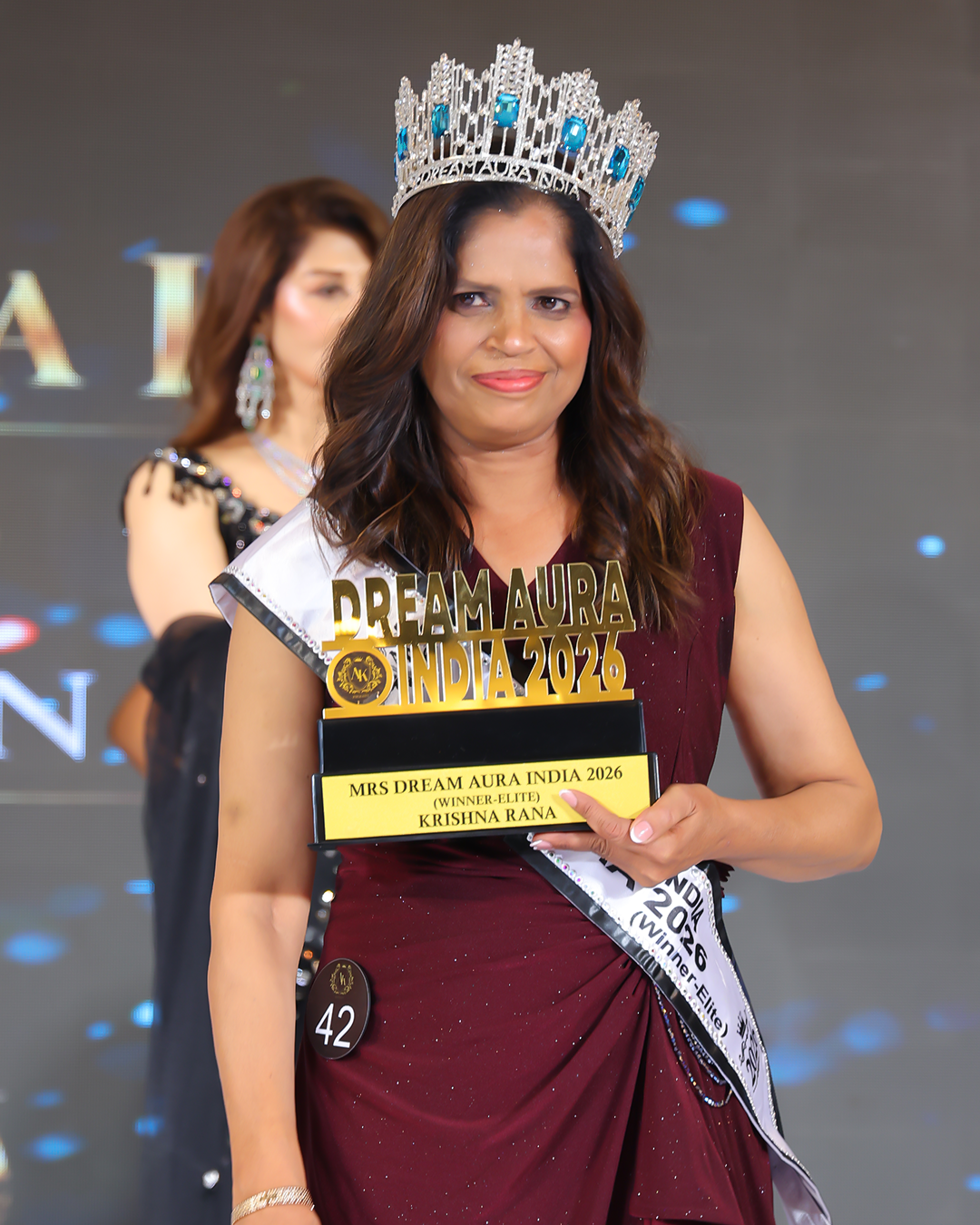 Krishna Rana poses outdoors wearing her crown and sash while holding the trophy as Mrs Dream Aura India Elite Winner 2026.