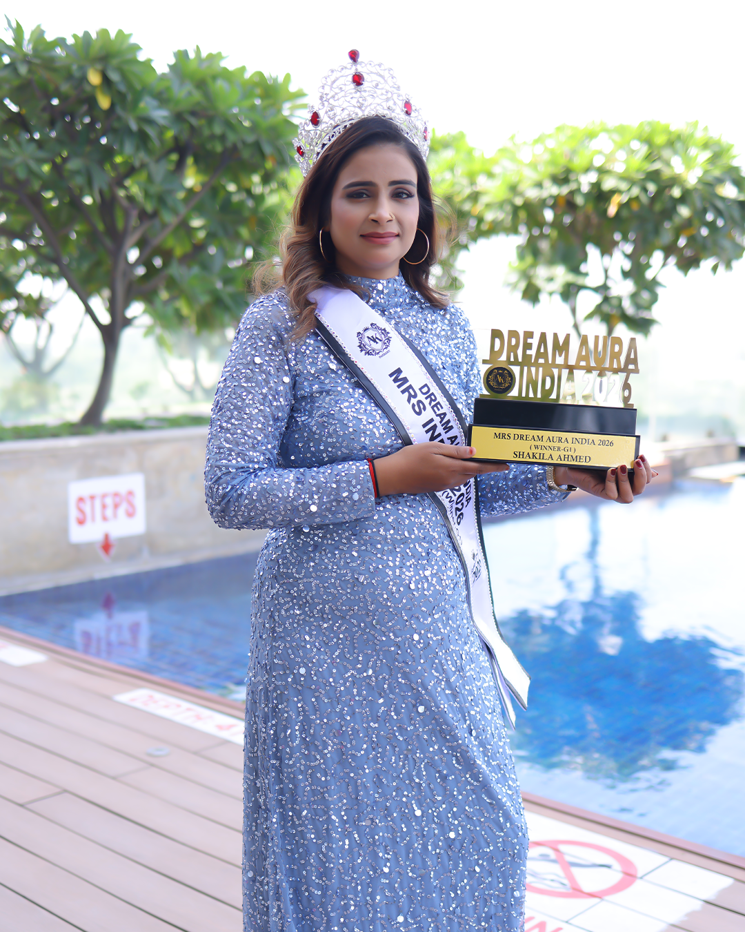 Shakila Ahmed holding the Dream Aura India 2026 G-1 Winner trophy wearing her crown and sash