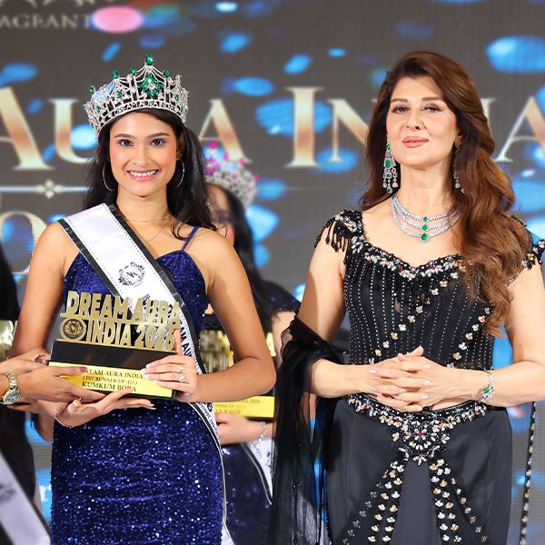 Kumkum Bora , First Runner-Up of Mrs Dream Aura India 2026 G-1 winner, wearing a blue embellished gown, crown, and sash while holding her award beside a celebrity guest at the pageant event.